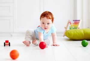 cute infant baby crawling on the floor at home, playing with colorful balls