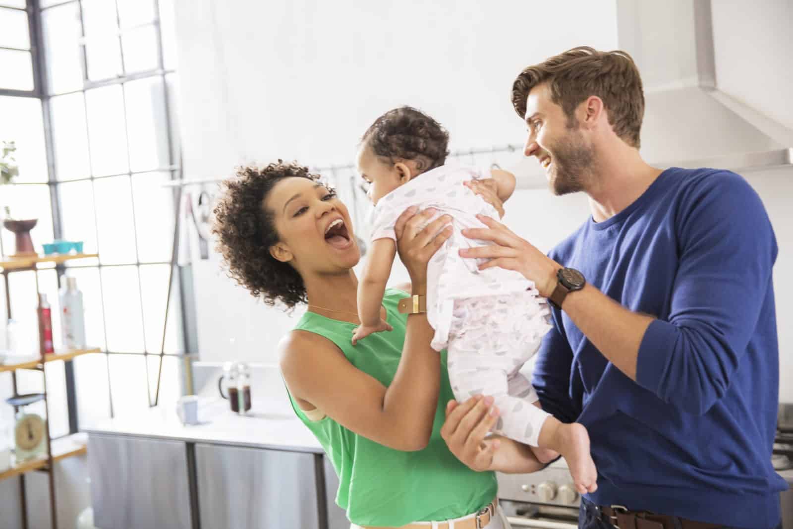 Happy parents holding their baby daughter in domestic kitchen