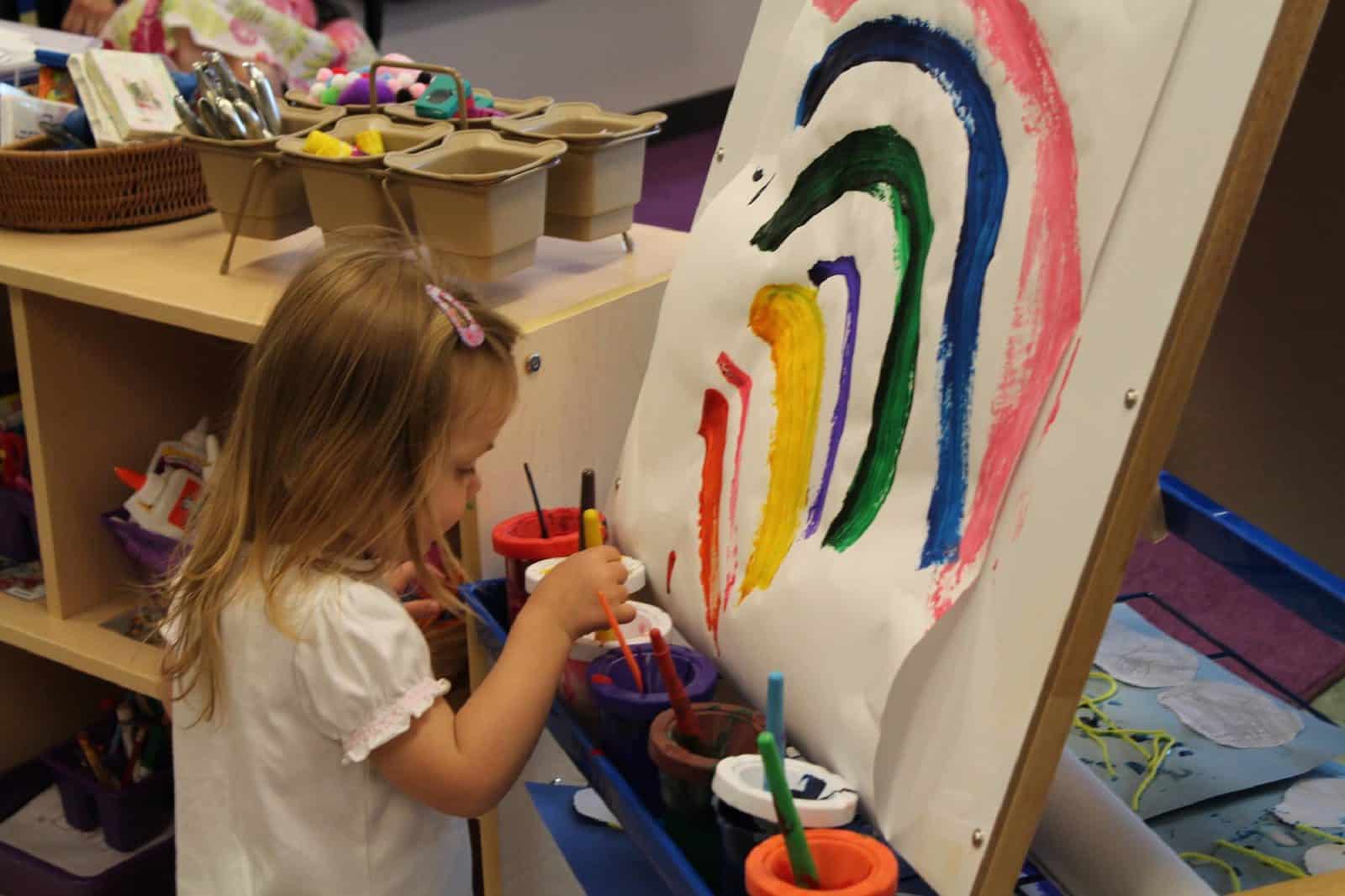 young girl painting rainbow on paper