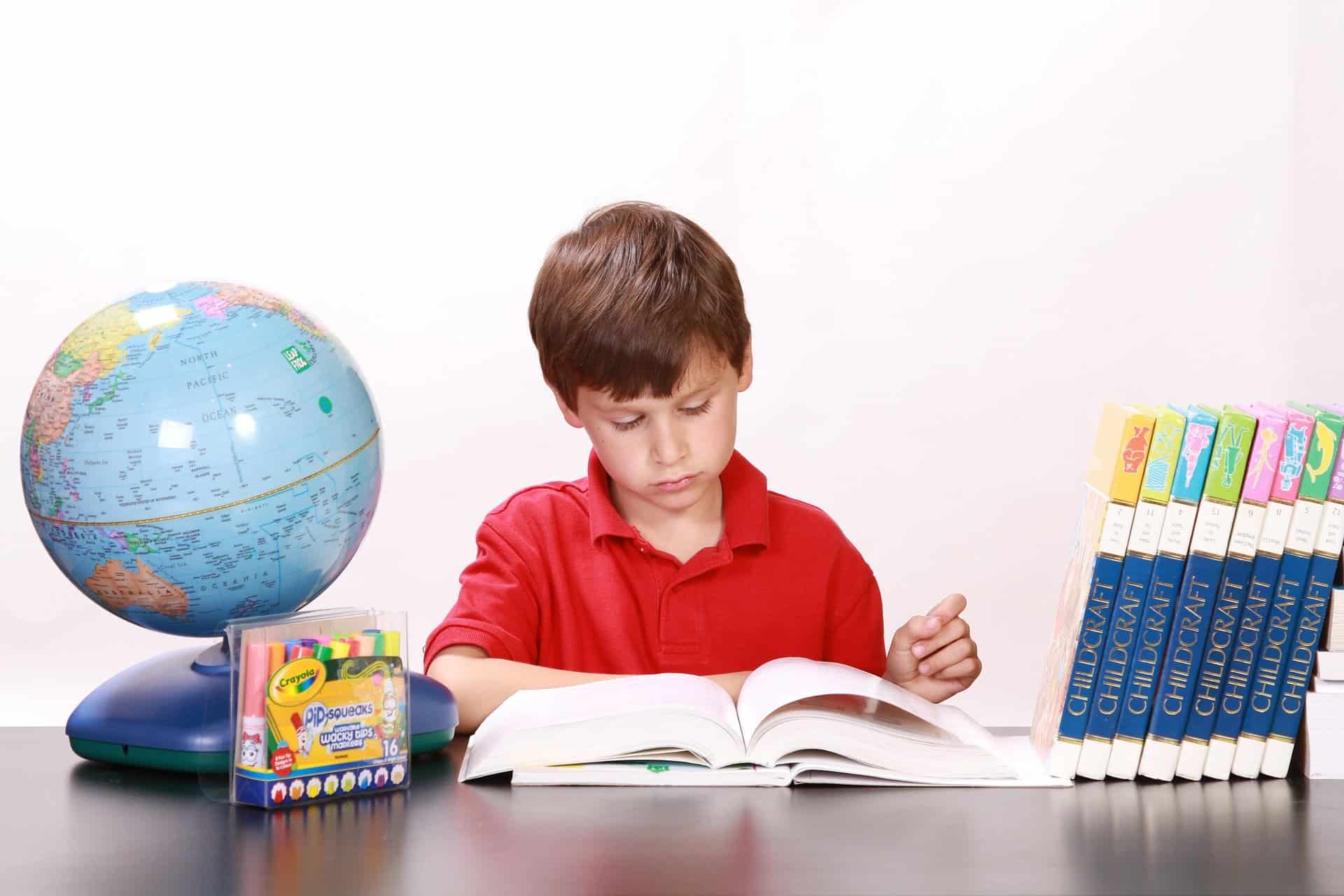 Child with a stack of books sitting at a desk and reading